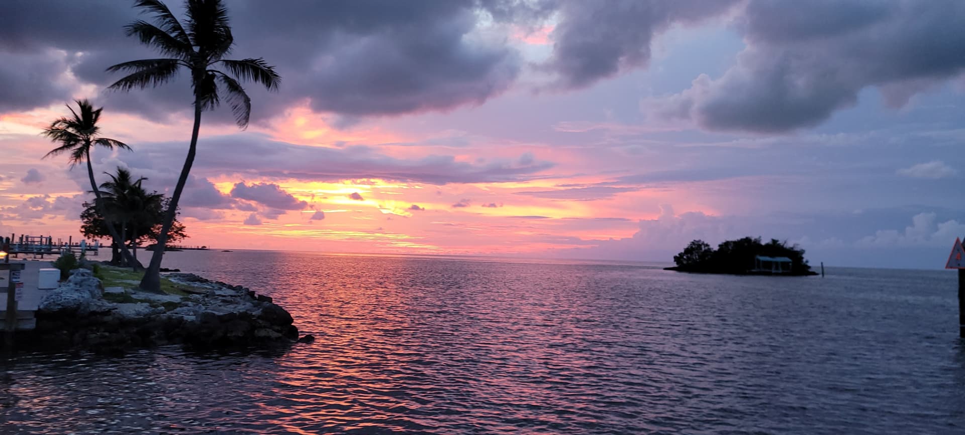 A waterfront at sunset, palms silhouetted over still water
